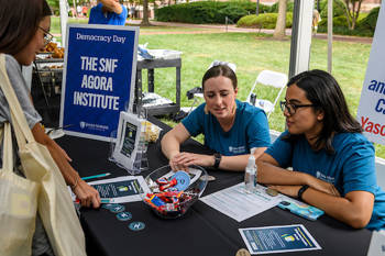 Two girls are sitting at the counter of THE SNF AGORA INSTITUTE and a woman is looking at the brochures on it